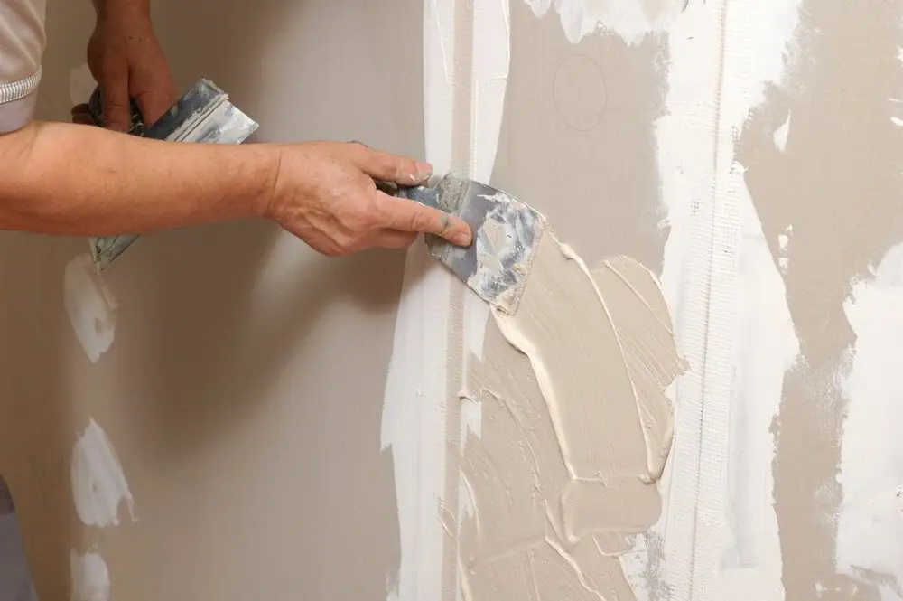 Drywall patch being checked with a work light held at a low angle