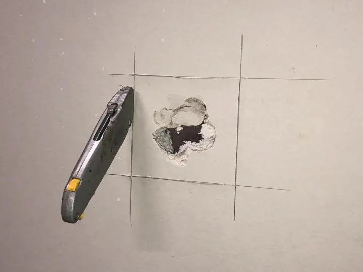 Hole in a drywall wall being prepared for a patch with a utility knife