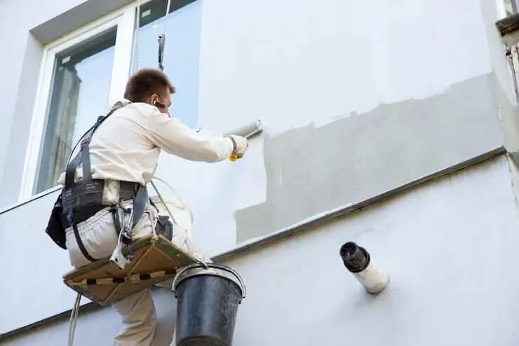 Painter applying a light-coloured coat to the exterior wall of a Florida home
